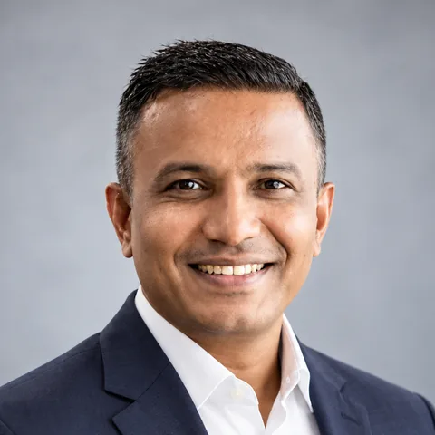 Satya Mehta, smiling, in a navy blazer and white shirt